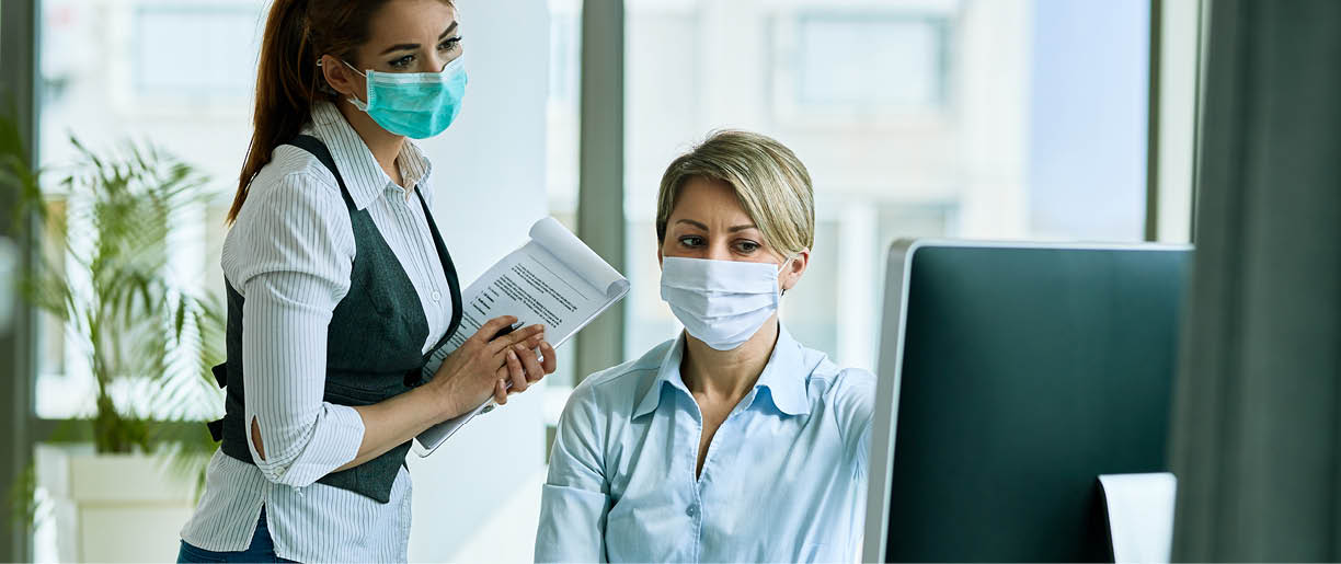 Female business colleagues with face masks working in the office and reading an e-mail on a computer  