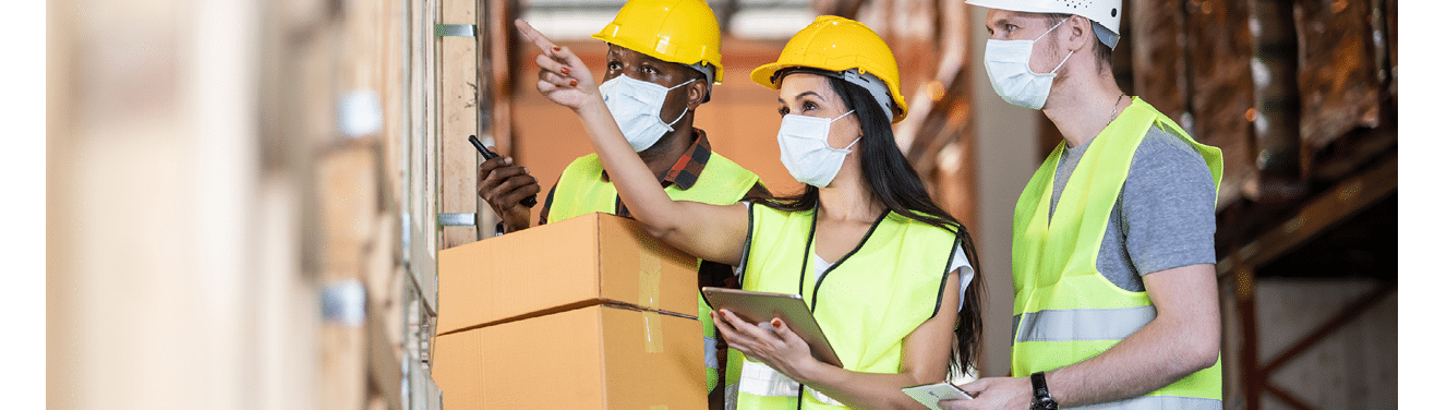 Woman worker hold tablet talking to man in warehouse store  Male and female engineers people wear safety hard helmet, vest and face mask checking storage box parcel in factory during covid 19 pandemic
