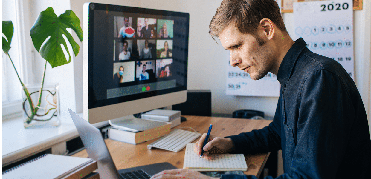 Man siting by desktop computer and making notes  Working remotely Young man having video call via computer in the home office  Stay at home and work from home concept  Managing business team meeting