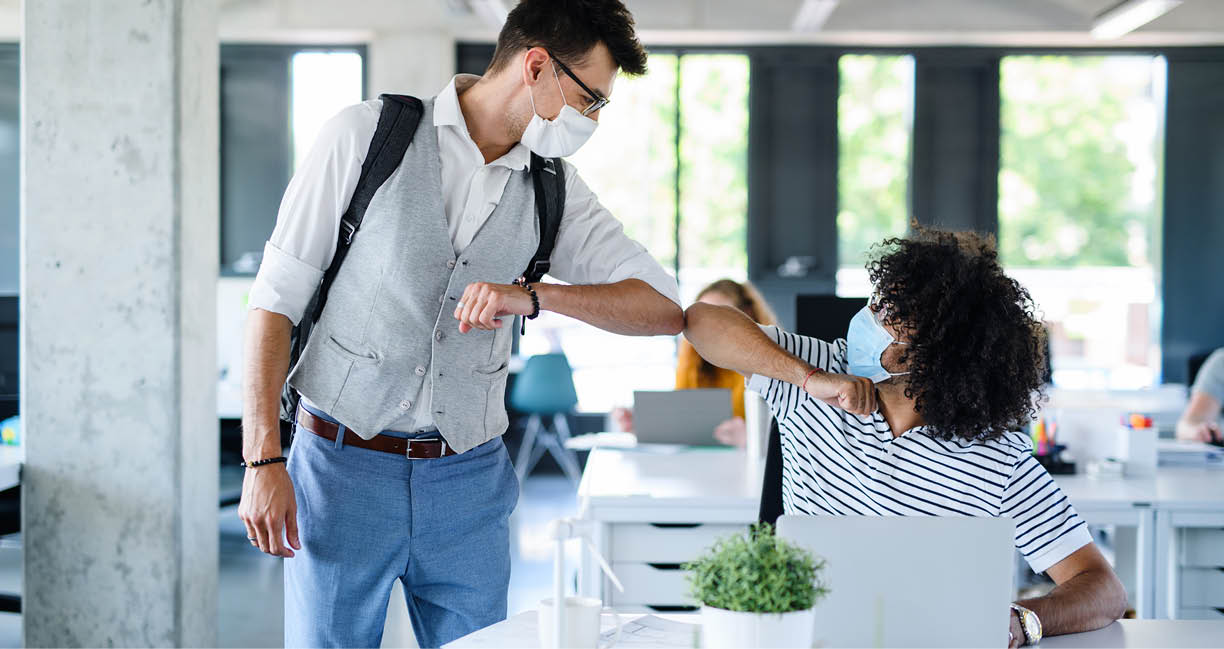 Young people with face masks back at work in office after lockdown, greeting 