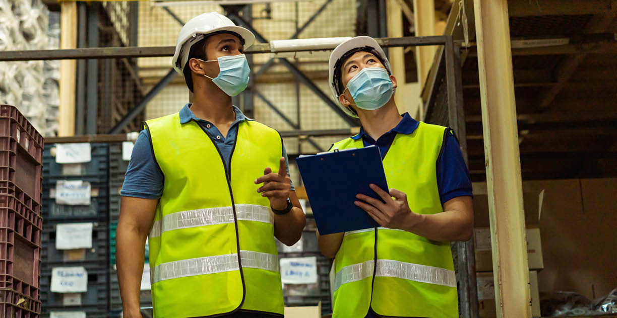 Group of young factory warehouse workers wearing a protective face mask while working in logistic industry indoor  Asian and Indian ethnic men checking item order during Coronavirus Covid 19 pandemic