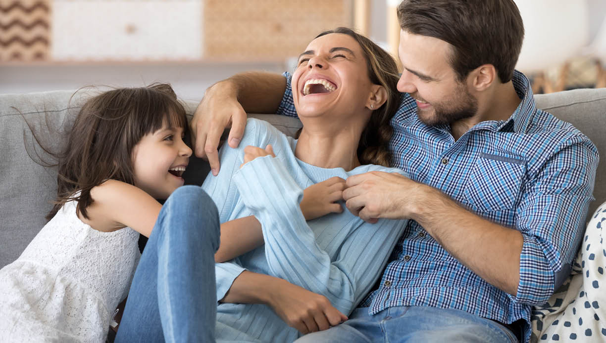 Cheerful people sitting on couch in living room have fun little daughter tickling mother laughing together with parents enjoy free time playing at home  Weekend activity happy family lifestyle concept