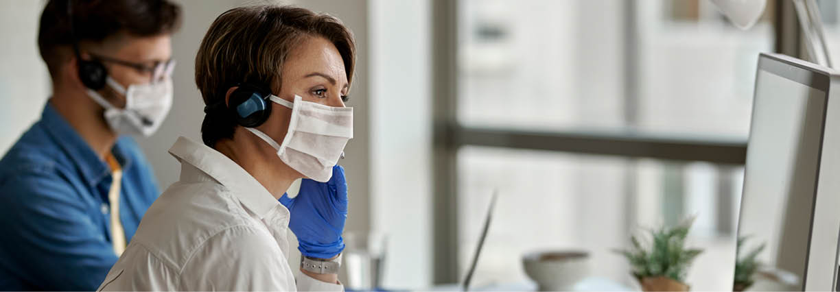 Call center agents wearing protective face masks while working on computer and communicating with customers during coronavirus epidemic  Focus is on woman  