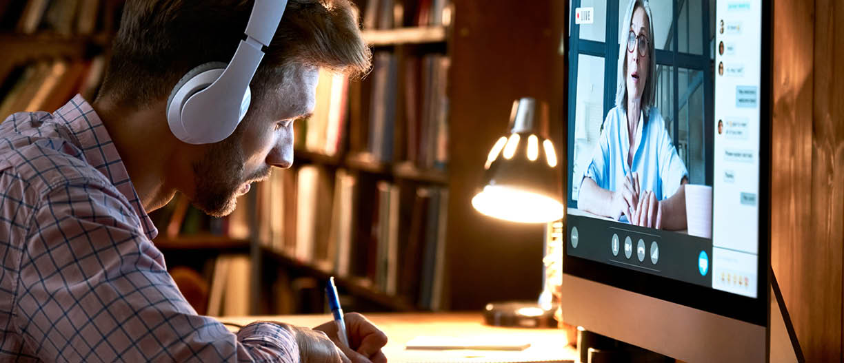 Male student wearing headphones conference video calling, watching webinar, online training class, virtual chat meeting with remote teacher or coach distance learning using computer, taking notes 